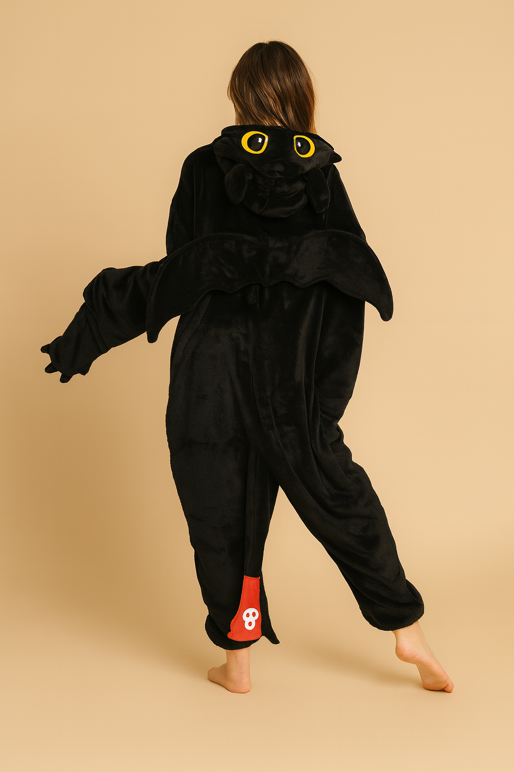 Person wearing a black dragon onesie with yellow eyes on a beige background